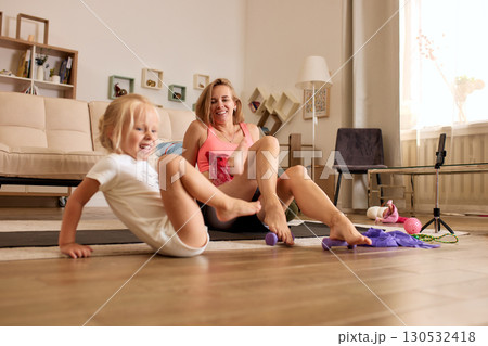 Mother and daughter exercising together in a cozy home living room 130532418