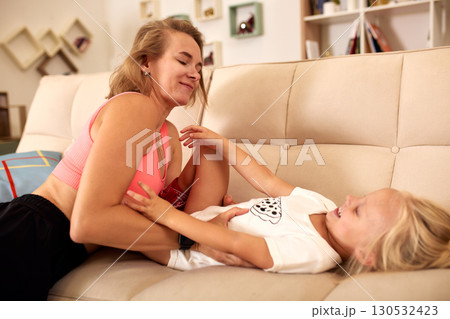 Mother and daughter laughing together on a cozy sofa at home Mother and daughter laughing together on a cozy sofa at home 130532423