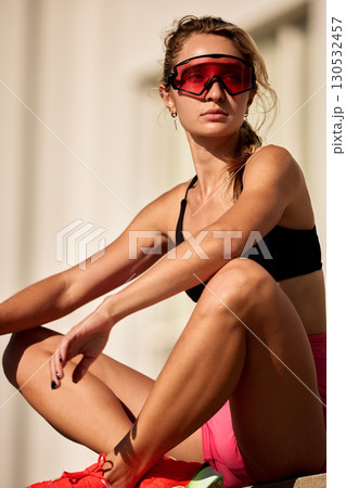 Athletic woman wearing red-tinted glasses taking a break in outdoor sunlight Athletic woman wearing red-tinted glasses taking a break in outdoor sunlight 130532457