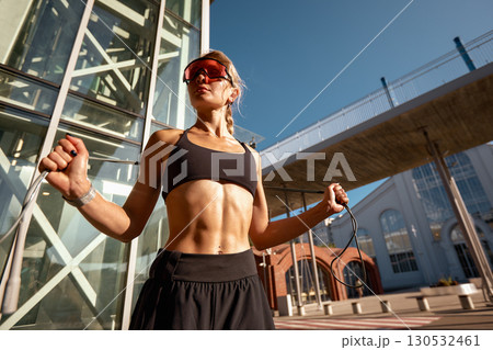 Athletic woman jump ropes outdoors near modern urban architecture Athletic woman jump ropes outdoors near modern urban architecture 130532461
