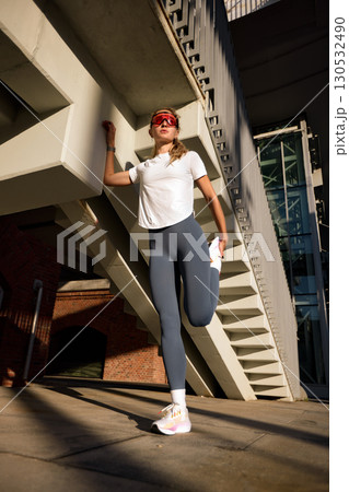 Young woman stretching outdoors near modern building on a sunny day 130532490