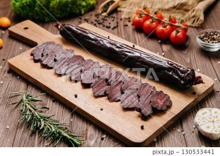 Sliced dry sausage on rustic wooden board with spices and tomatoes, top view 130533441