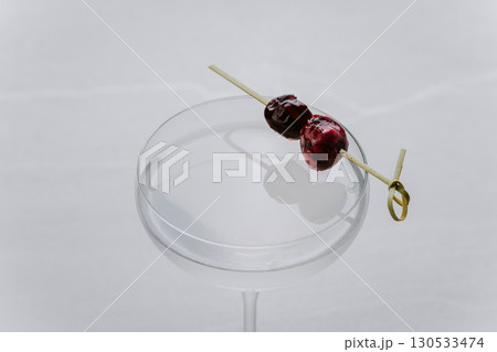 Minimalist clear cocktail in a coupe glass with cherries on skewer on light background Minimalist clear cocktail in a coupe glass with cherries on skewer on light background 130533474