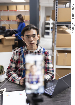 Small business owner uses a smartphone to film content inside fulfillment center, vlog highlighting inventory, order processing and local delivery services for regional online promotion. Small business owner uses a smartphone to film content inside fulfillment center, vlog highlighting inventory, order processing and local delivery services for regional online promotion. 130533657