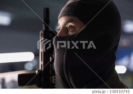 Close up of terrorist wearing mask holding rifle, prepared to start guerilla warfare operation against enemies. Rebel forces insurgent with weapon in hidden base starting offensive against opponents 130533743