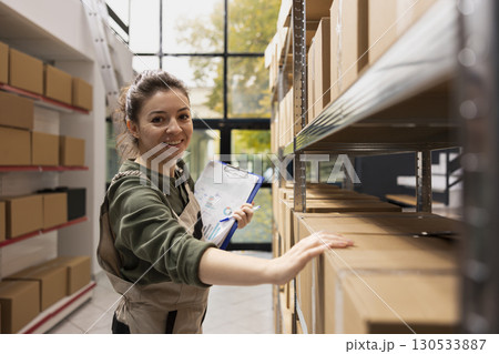 Portrait of worker preparing cardboard boxes for dispatch in small scale warehouse, handling product retail orders, shipment service operations and e-business activity. Small delivery. 130533887