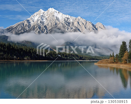 Snowy mountain and calm lake with pine forest reflection and morning fog panoramic nature landscape 130538915