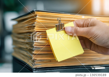 Hand Placing Sticky Note on Document Stack During Validation Process in Office Environment 130539189