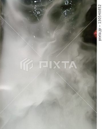 Swirling mixture of white and gray smoke or vapor creating abstract pattern, with hints of dark background and subtle reflections, evoking 130540852