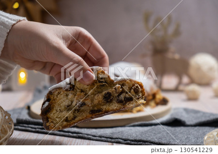 Woman taking slice of Traditional German Christmas stollen cake in background of handmade festive decor. Winter holiday treats. Vegan baking recipe 130541229