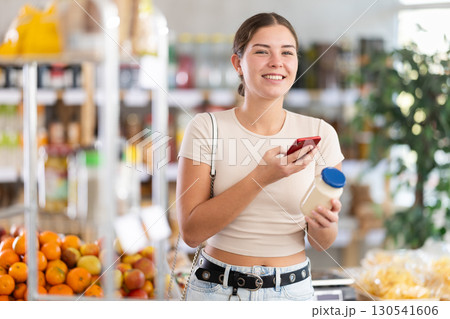 European young woman customer at shop scans QR code on mayonnaise bottle using phone camera European young woman customer at shop scans QR code on mayonnaise bottle using phone camera 130541606