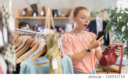 Surprised teenage girl scanning QR-code on handbag in clothing store 130541719