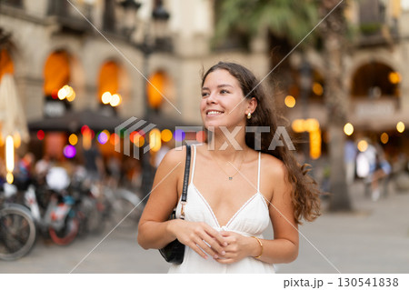 In evening, young smiling girl walks along city street Placa Real In evening, young smiling girl walks along city street Placa Real 130541838