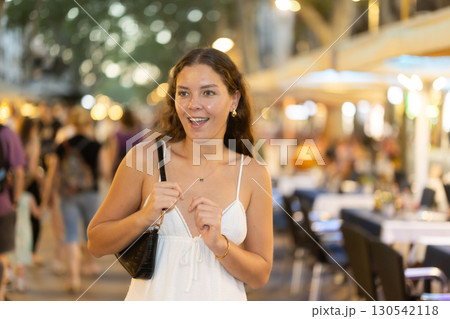 In evening, young smiling girl walks along city street La Rambla 130542118