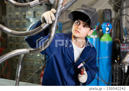 Young welder inspecting weld seam on metal pipe structure Young welder inspecting weld seam on metal pipe structure 130542242