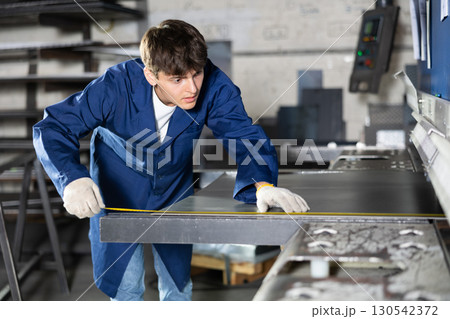 Guy measuring sheet of metal with tape measure Guy measuring sheet of metal with tape measure 130542372