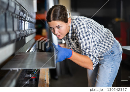 Young woman bends sheet of metal under pressure Young woman bends sheet of metal under pressure 130542557