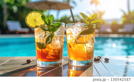 An iced citrus cocktail with mint and lime sits on the edge of a cool pool, a refreshing summer beverage 130542587