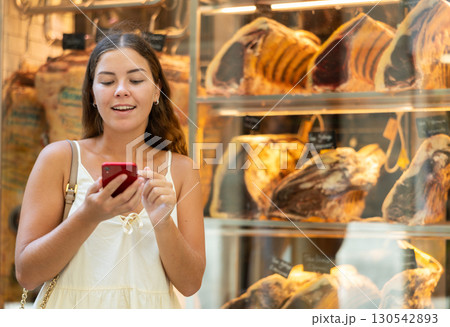 Portrait of young girl with smartphone choosing delicacy of exquisite dry-aged beef at showcase 130542893
