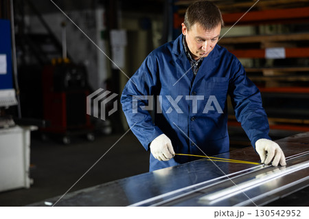 Worker applying markings on steel sheet in metal workshop 130542952