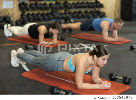 Energetic young woman doing plank near other people in gym Energetic young woman doing plank near other people in gym 130542975