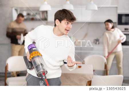 Guy vacuuming floor while his relatives help tidy up room 130543025