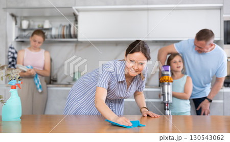 Woman rubbing table in kitchen while cleaning house with family Woman rubbing table in kitchen while cleaning house with family 130543062