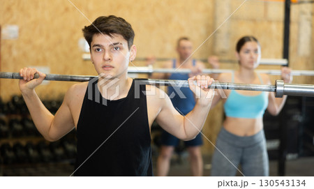 Young male bodybuilder performing strength and endurance exercises during group barbell lifting in CrossFit class Young male bodybuilder performing strength and endurance exercises during group barbell lifting in CrossFit class 130543134