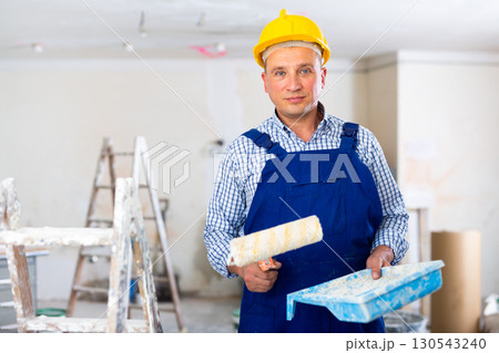 Portrait of positive man painter in a protective helmet and overal with paint roller 130543240