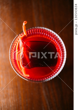 Citrus cocktail. Refreshing liquor. Bright aromatic negroni in glass. Alcoholic red drink ice cube orange fruit slice on pub table. 130543634
