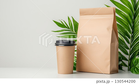 Eco-Friendly Coffee Cup and Paper Bag Surrounded by Lush Green Tropical Leaves 130544200