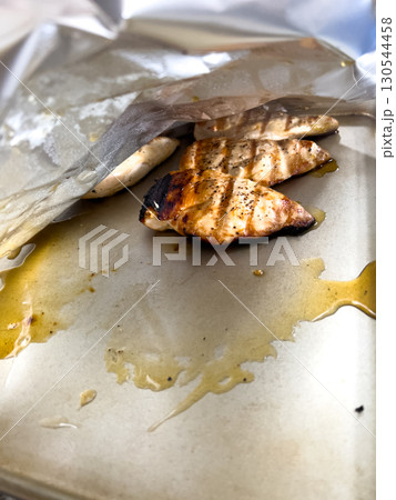 Grilled chicken breasts rest on a foil-lined baking sheet, still showing char marks and slight juices around the edges. The lighting is natural and the scene captures the texture of cooked meat. 130544458