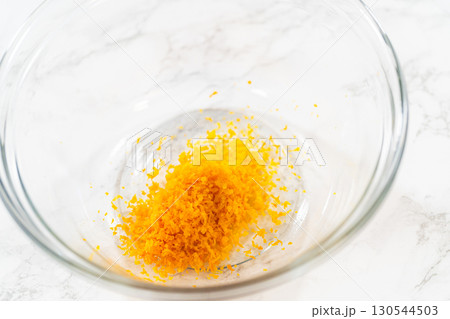 A closeup of bright orange zest in a glass bowl, which will add a zesty flavor to the Zesty Orange Gingerbread Cookie Dough. This fresh zest is key to enhancing the dough citrusy undertone. 130544503