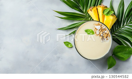 Creamy Tropical Smoothie with Pineapple Slices and Fresh Green Leaves on a Light Background 130544582
