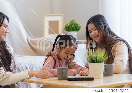During a warm winter day a child enjoys drawing while sitting with two adults at a table with beverages and a plant, showcasing a moment of creativity and connection indoors. 130545290