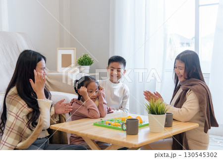 During winter, a family enjoys time together indoors playing a board game at a small table, creating a warm and happy moment, as they celebrate a fun winter day together. 130545302