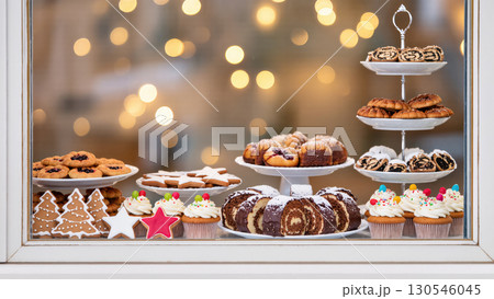 Christmas pastry shop window with festive desserts, cupcakes, cookies, and sweet rolls displayed behind glass with glowing lights 130546045