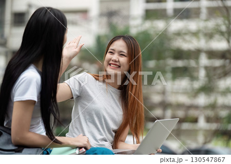 Cheerful students celebrating collaboration with a high-five in an outdoor study space 130547867