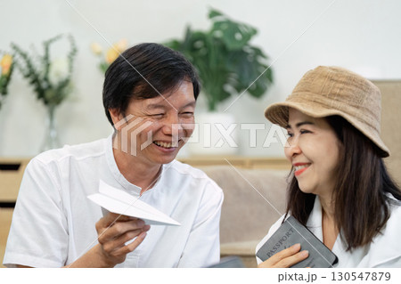 Senior couple excitedly discussing travel plans while holding a passport and paper airplane. Senior couple excitedly discussing travel plans while holding a passport and paper airplane. 130547879