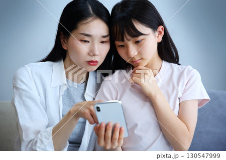 スマホを真剣に見る母と娘のイメージ スマホを真剣に見る母と娘のイメージ 130547999