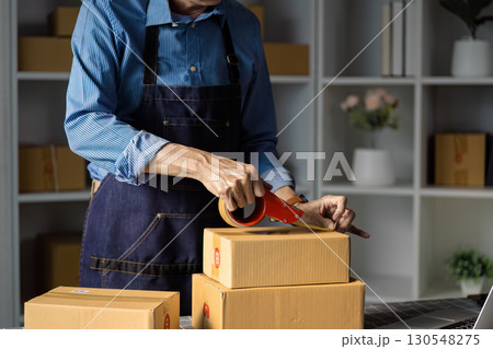 E-commerce worker packing boxes for online sales with tape in a workspace. E-commerce worker packing boxes for online sales with tape in a workspace. 130548275