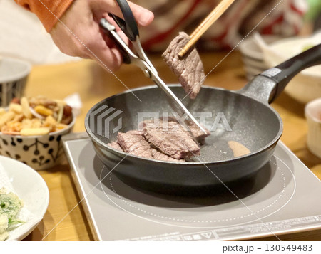 肉をフライパンの上でハサミで切る手元 130549483