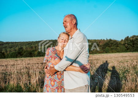 Happy senior couple embracing in meadow at sunset. Happy senior couple embracing in meadow at sunset. 130549553