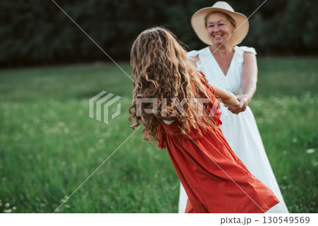 Grandma and girl holding hands and dancing in the middle of meadow. 130549569