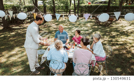 Areal view of grandparents, parents and kids dining together outside. Areal view of grandparents, parents and kids dining together outside. 130549631