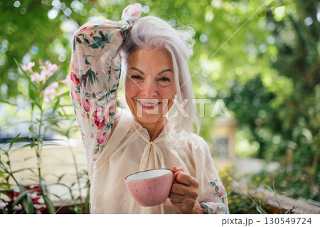 Portrait of beautiful senior woman standing on balcony, drinking coffee. 130549724