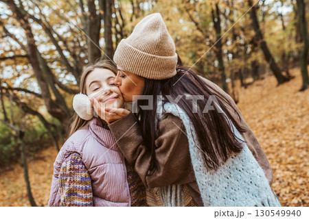 Mother kissing daughter on cheek during walk in autumn nature. 130549940