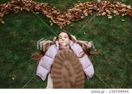 Portrait of teen girl laying on grass in the middle of autmn leaves. Portrait of teen girl laying on grass in the middle of autmn leaves. 130549944