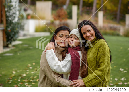 Mother, grandmother and granddaugter standing in autumn garden. 130549960