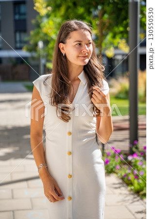 Young woman wearing a white midi dress walking outdoors in Old Money style. Concept of timeless fashion, graceful femininity and understated elegance in modern lifestyle. 130550530